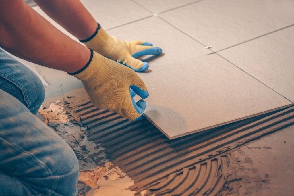 Worker installing ceramic floor tiles using adhesive mortar layer
