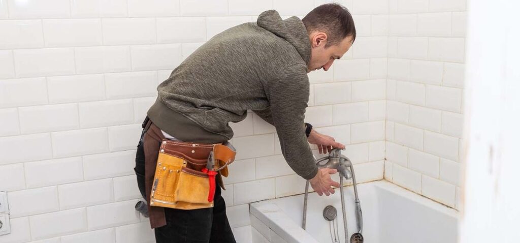 Plumber repairing bathtub faucet during home bathroom renovation